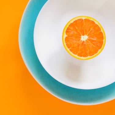 Half an orange on a white plate in a teal bowl